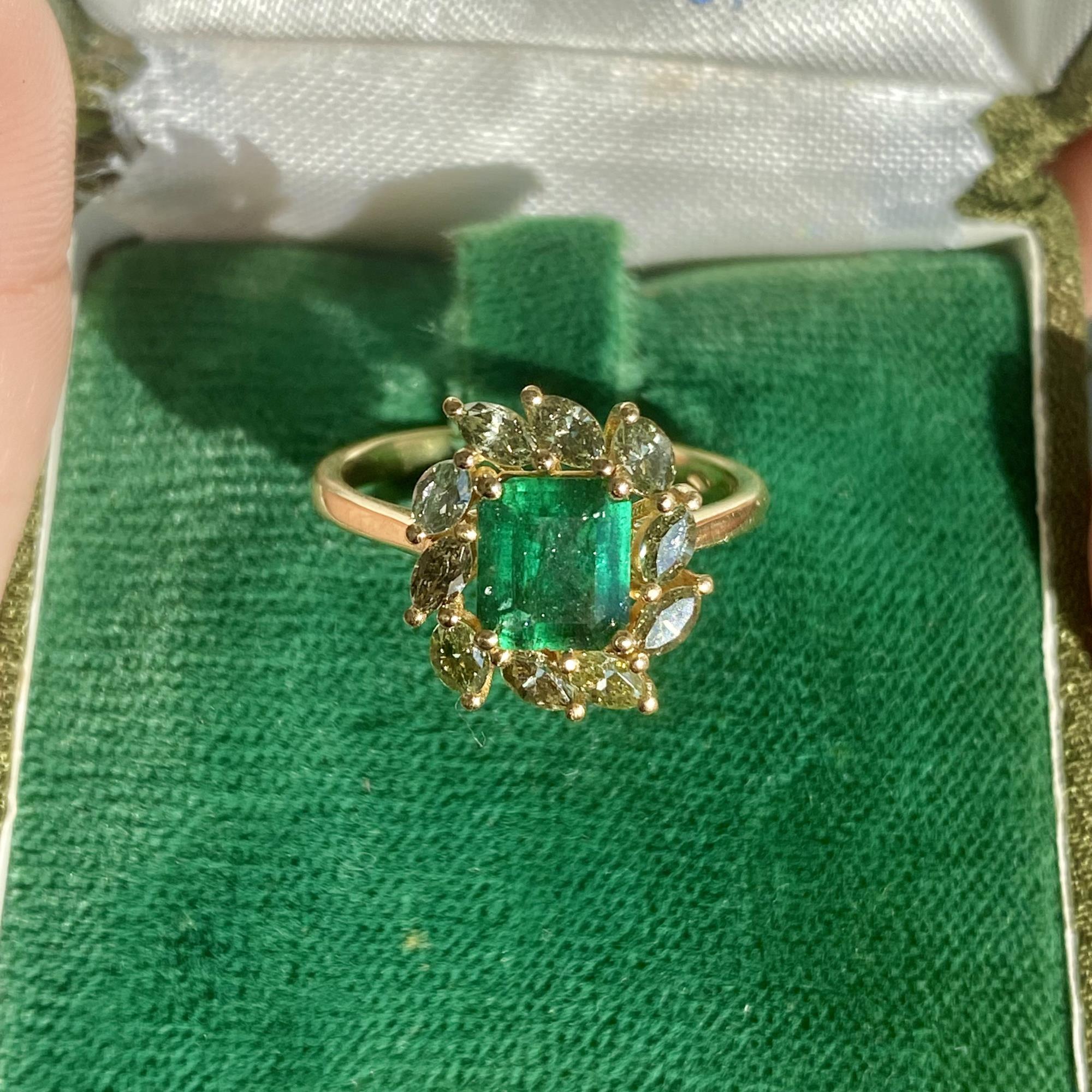 Vintage daisy ring with an emerald weighing approx 0.85 ct and grey diamonds totaling approx 0.75 ct.